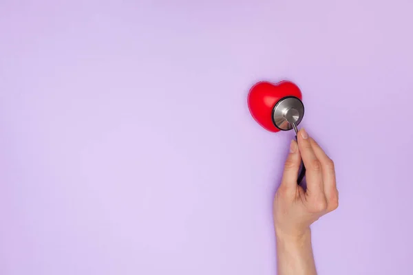 听诊器 红色的心脏和紫色背景的文字空间 女医生用听诊器听工作的心脏 健康保险概念 — 图库照片