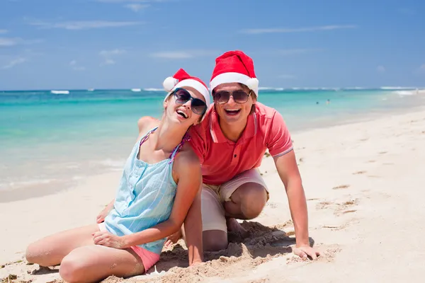 Młoda para w santa kapelusze śmiejąc się na tropikalnej plaży. Nowy rok — Zdjęcie stockowe