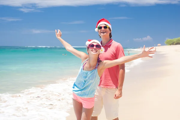 Casal jovem em chapéus de santa rindo na praia tropical. ano novo — Fotografia de Stock