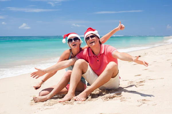 Giovane coppia in cappelli di Babbo Natale ridere sulla spiaggia tropicale. nuovo anno — Foto Stock