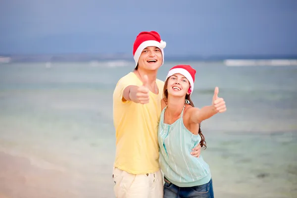 Pareja joven con sombreros de Santa Claus riendo en la playa tropical. año nuevo — Foto de Stock