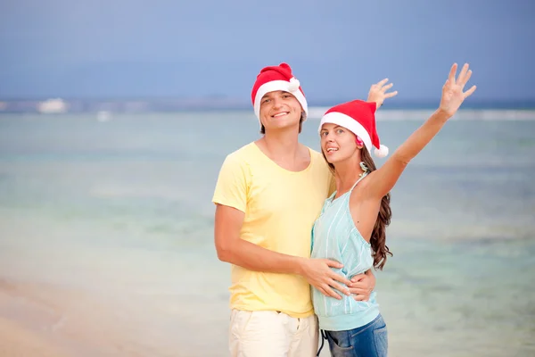 Pareja joven con sombreros de Santa Claus riendo en la playa tropical. año nuevo — Foto de Stock