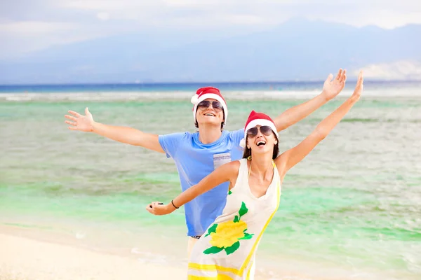 熱帯のビーチで笑いながらサンタ帽子の若いカップル。新しい年 — ストック写真
