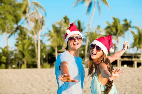 Pareja joven con sombreros de Santa Claus riendo en la playa tropical. año nuevo —  Fotos de Stock