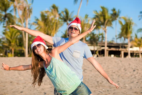 Casal jovem em chapéus de santa rindo na praia tropical. ano novo — Fotografia de Stock