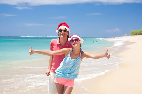 Jeune couple en chapeaux de Père Noël riant sur la plage tropicale. nouvel an — Photo