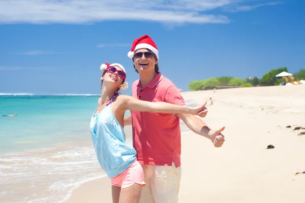 Jeune couple en chapeaux de Père Noël riant sur la plage tropicale. nouvel an — Photo