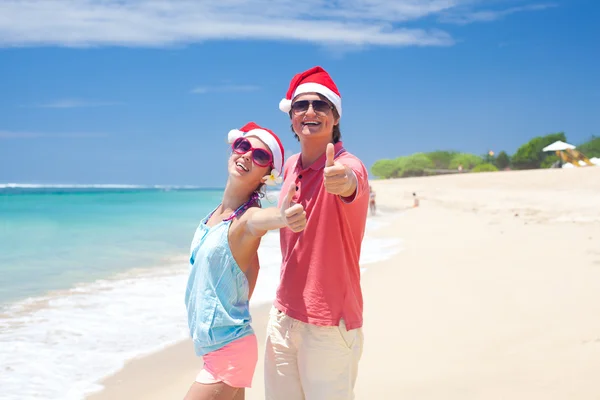 Casal jovem em chapéus de santa rindo na praia tropical. ano novo — Fotografia de Stock
