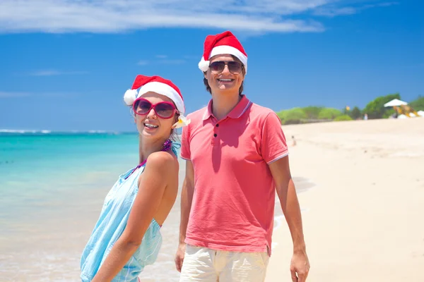 Mladý pár v santa klobouky, směje se na tropické pláži. Nový rok — Stock fotografie