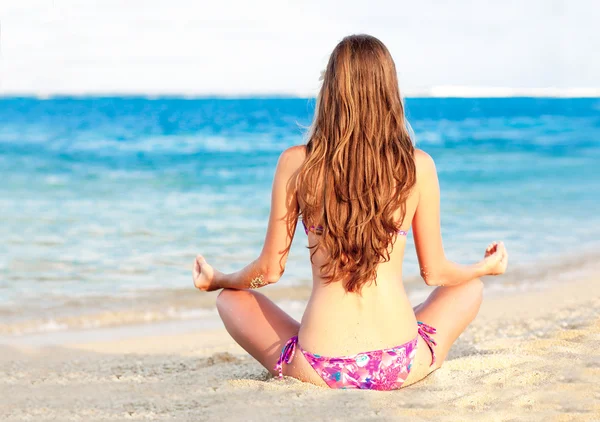 Ragazza dai capelli lunghi in bikini in posa di loto sulla spiaggia tropicale di bali — Foto Stock
