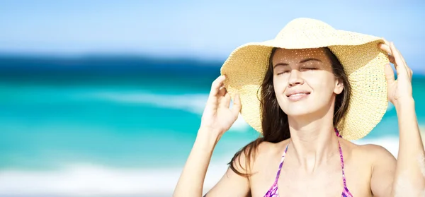 Счастливая молодая женщина улыбается в соломенной шляпе с закрытыми глазами на пляже — стоковое фото