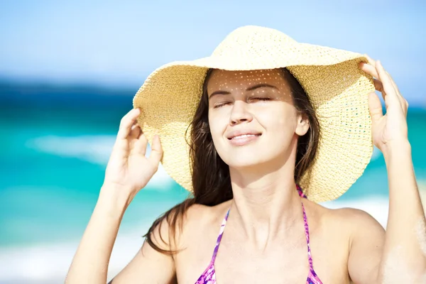 Gelukkig jonge vrouw die lacht in stro hoed met gesloten ogen op het strand — Stockfoto