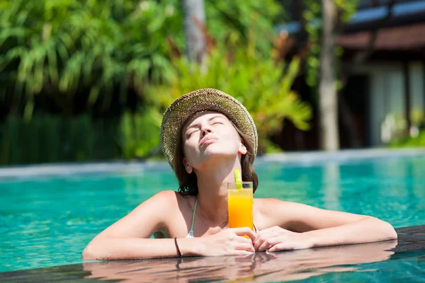 Bela mulher em chapéu de palha com suco fresco na piscina de luxo — Fotografia de Stock