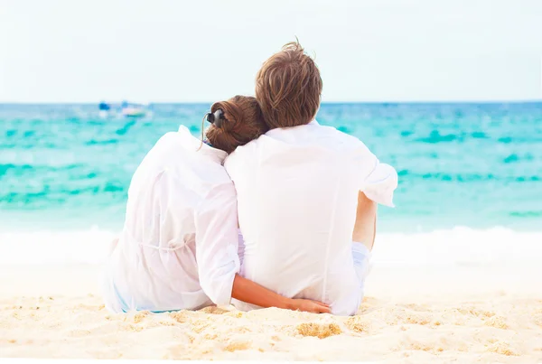 Bakifrån unga lyckliga paret sitter på tropical beach. smekmånad koncept — Stockfoto