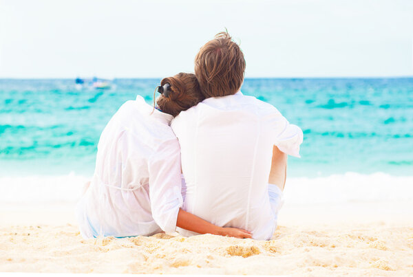 Back view of young happy couple sitting on tropical beach. honeymoon concept