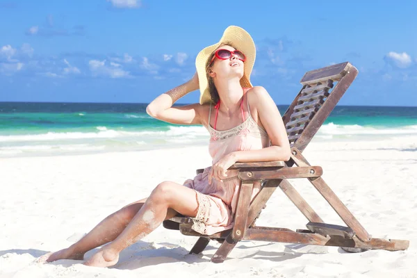 Ung kvinna i stråhatt och bikini sitter på strandstol — Stockfoto