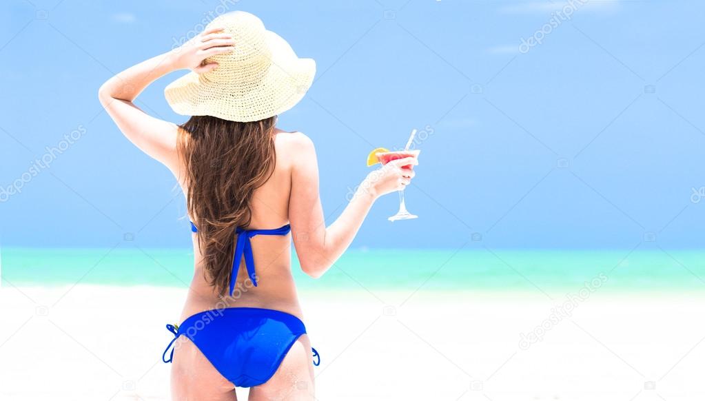 Woman in straw hat and bikini enjoying cocktail on beach