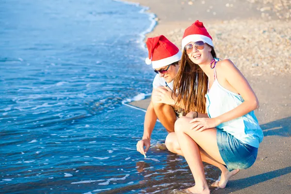 Casal jovem em chapéus de santa rindo na praia tropical. ano novo — Fotografia de Stock