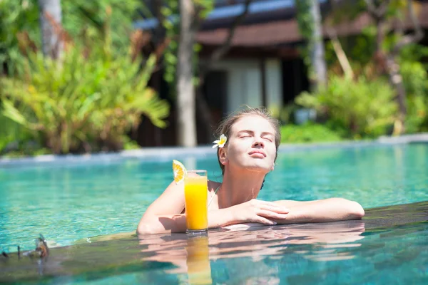 Beautiful girl with orange juice in luxury pool — Stock Photo, Image