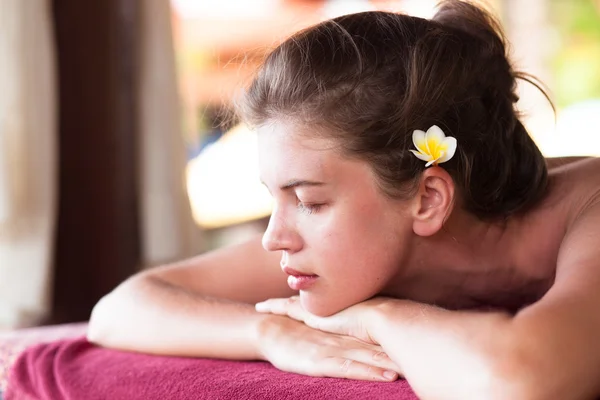 Bella giovane donna con fiore in capelli sdraiato in spa — Foto Stock