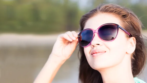 Porträtt av ung kvinna i rosa solglasögon leende på stranden Stockbild