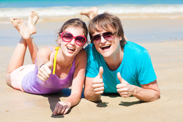 Closeup of happy young couple in sunglasses lying on beach smiling