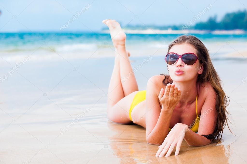 Long haired girl in sunglasses blowing a kiss on tropical beach