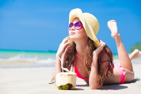 Jonge vrouw glimlachen liggend in stro hoed in zonnebril met kokosnoot op het strand — Stockfoto