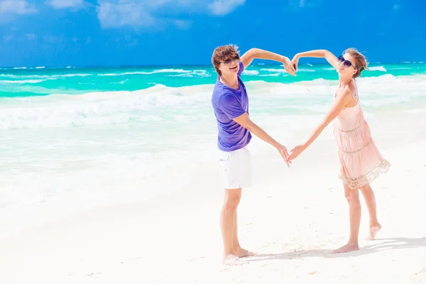 Jovem casal feliz na lua de mel fazendo a forma do coração na praia tropical — Fotografia de Stock