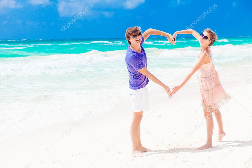 Young happy couple on honeymoon making heart shape on tropical beach