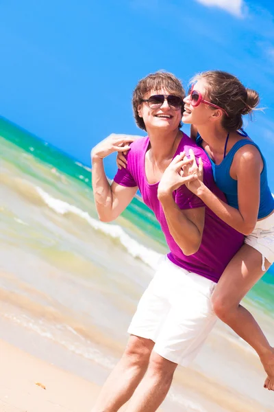 Happy couple piggybacking cheerful on beach on vacation — Stock Photo, Image