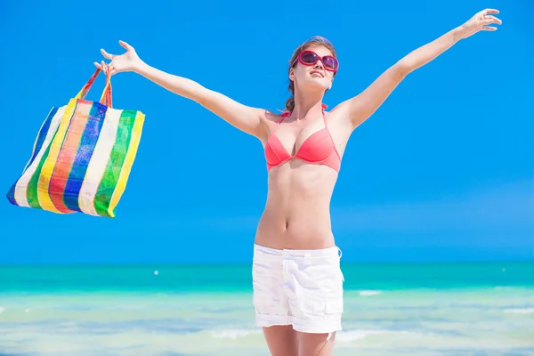 Woman in bikini and sunglasses with beach bag cheerful on beach — Stock Photo, Image