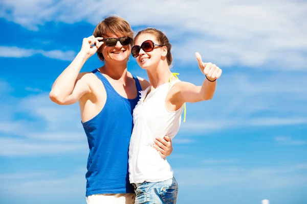 Jovem casal feliz em óculos de sol sorrindo apontando para o céu — Fotografia de Stock