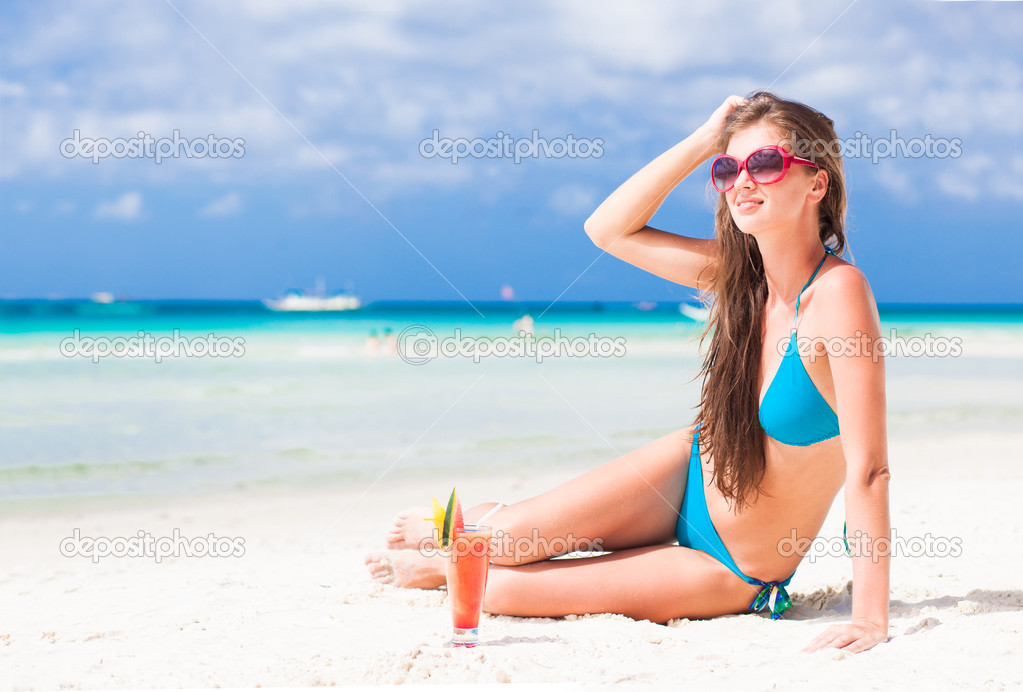 Woman in bikini and sunglasses with fresh watermelon juice on tropical beach