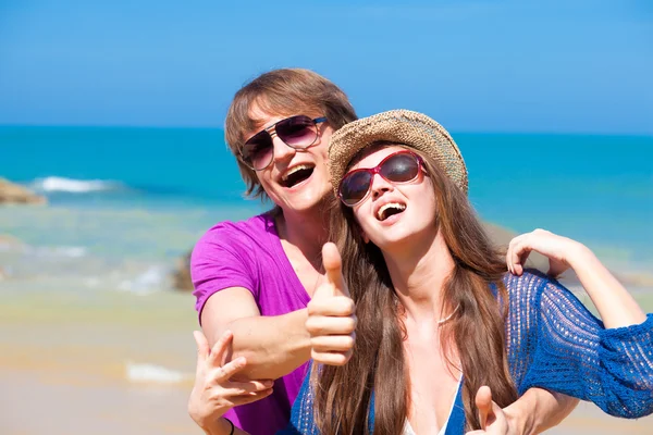 Vista frontale della giovane coppia felice in occhiali da sole che si abbraccia sulla spiaggia tropicale — Foto Stock