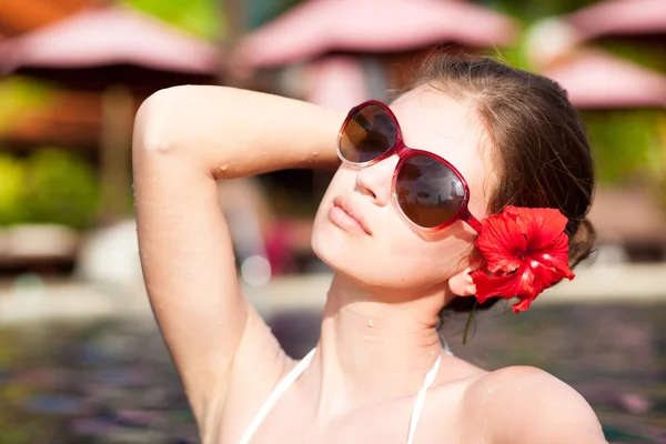 Krásná mladá žena v sluneční brýle s květinou ve vlasech v luxusní bazén — Stock fotografie