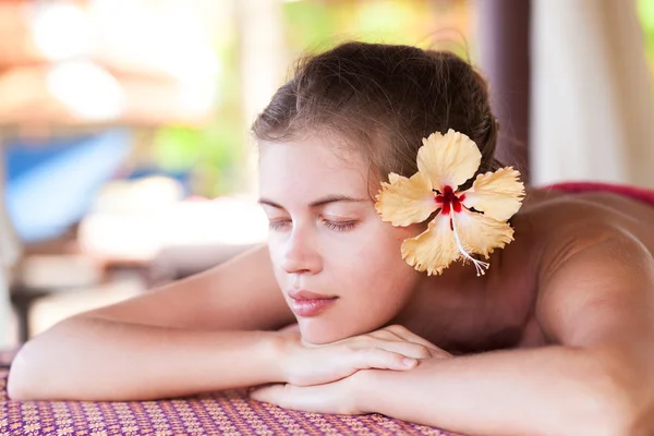 Mooie jonge vrouw met gele bloem in haar liggen in spa — Stockfoto