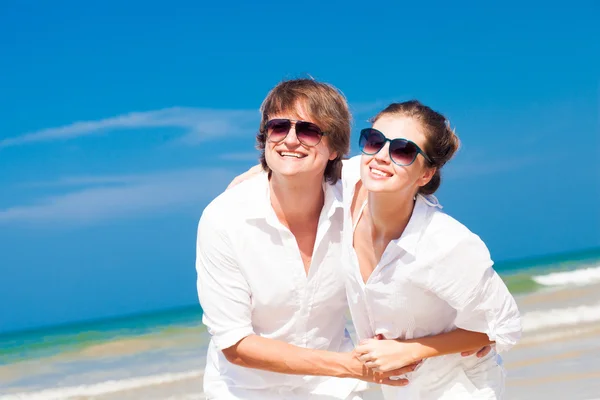 Primo piano di felice giovane coppia in abiti bianchi e occhiali da sole sorridente sulla spiaggia — Foto Stock