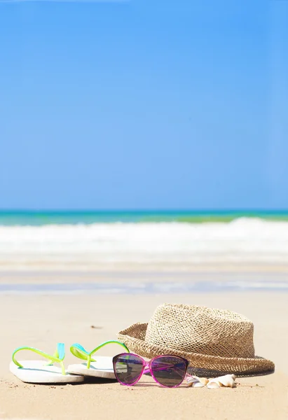 Flip flops straw hat and sunglasses on tropical beach with waves on background — Stock Photo, Image