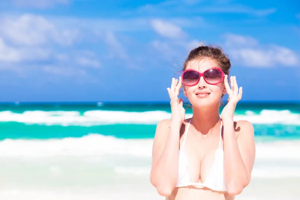 Vue de face de belle jeune femme en lunettes de soleil debout sur la plage tropicale profitant du soleil — Photo
