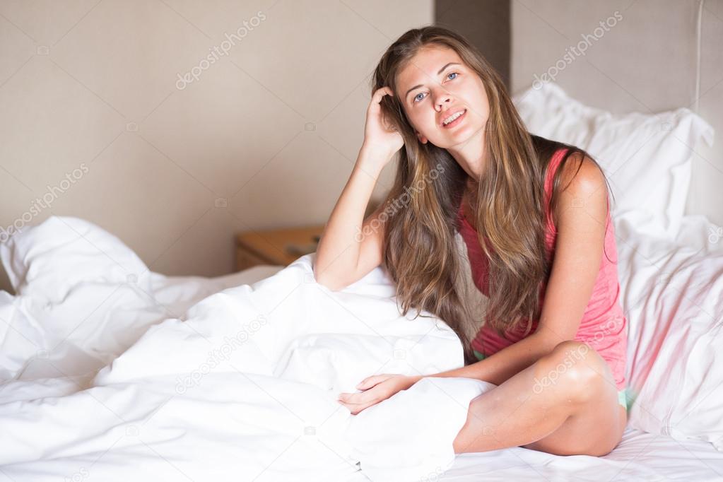 Beautiful happy young long haired woman waking up in the morning and smiling sitting on bed at home