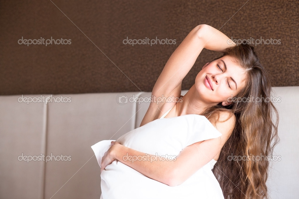 Beautiful happy young long haired woman waking up in the morning and smiling sitting on bed at home