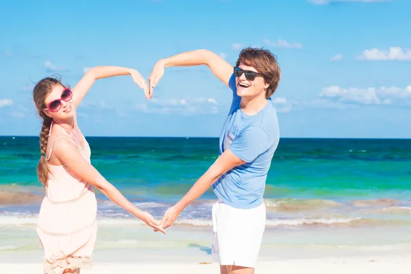 Giovane coppia felice facendo forma di cuore sulla spiaggia tropicale. luna di miele — Foto Stock