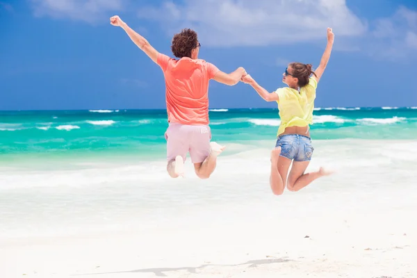 Pareja joven en ropa brillante saltando en la playa mirando en el horizonte —  Fotos de Stock