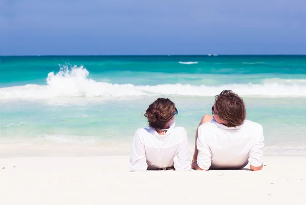 Vista posterior feliz pareja joven en ropa blanca en gafas de sol tumbado en la playa —  Fotos de Stock