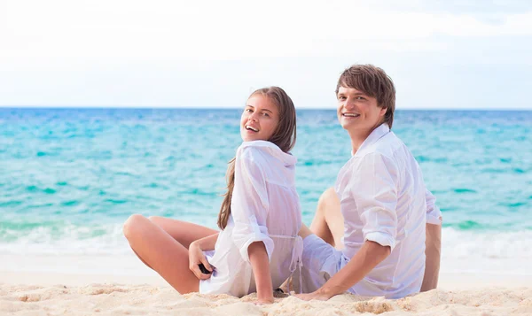 Εξωτερική άποψη του happy νεαρό ζευγάρι με λευκά ρούχα σε γυαλιά ηλίου που κάθεται στην παραλία — Φωτογραφία Αρχείου