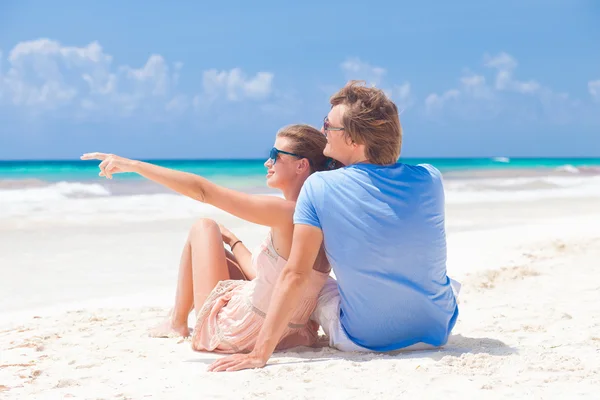 Framifrån lyckliga unga par i ljusa kläder i solglasögon liggande på stranden — Stockfoto