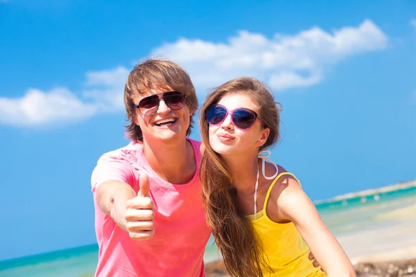 Vorderseite des glücklichen jungen Paares am Strand lächelnd und umarmt. Daumen hoch — Stockfoto