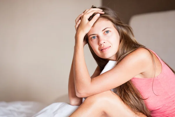 Mooi slaperig langharige jongedame ontwaken in de ochtend en glimlachend zittend op bed thuis — Stockfoto