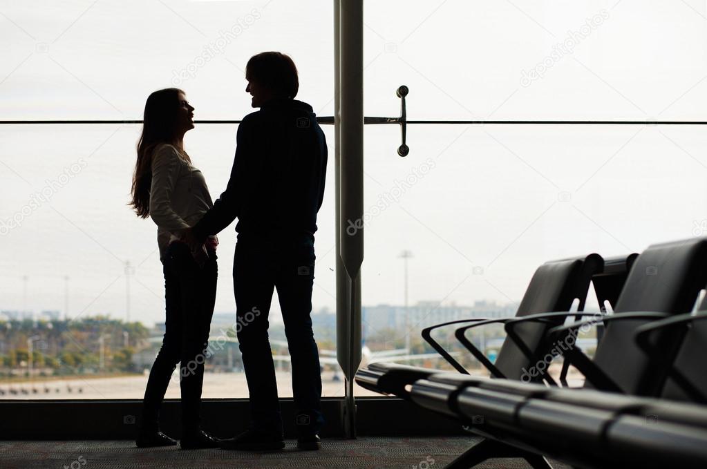 Silhouette of a couple holding hands, looking at each other and waiting at airport terminal